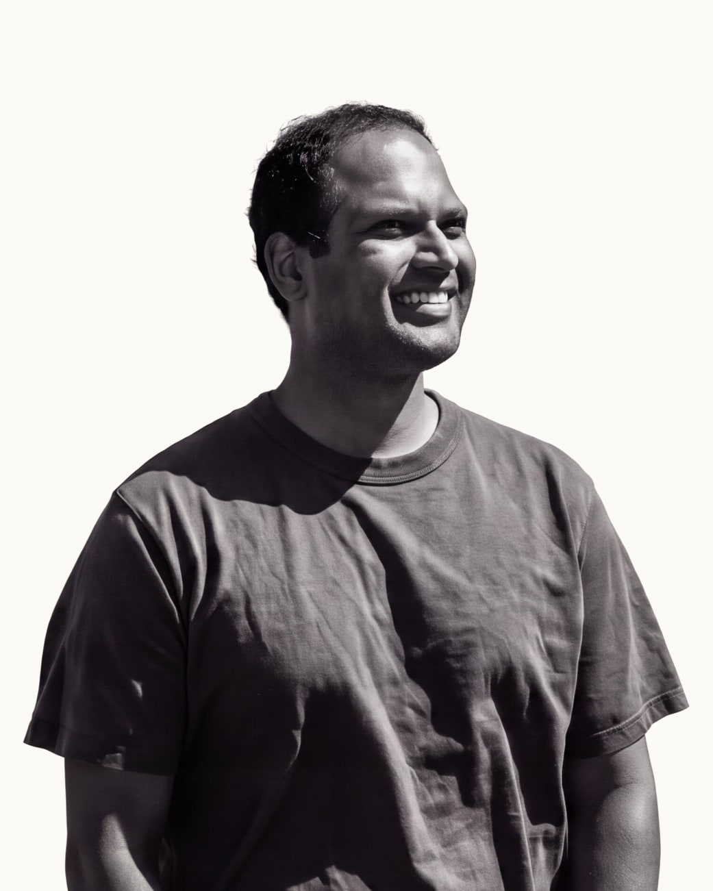 Jay Rao smiling and looking off to one side, in a dark t-shirt, photographed in black and white against a white sky