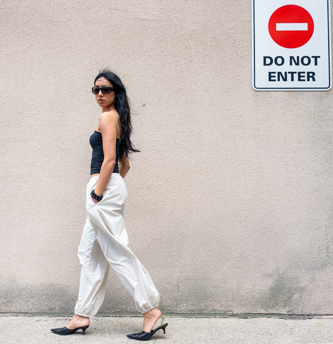 Model in profile and sunglasses walking past a pale wall in black heels