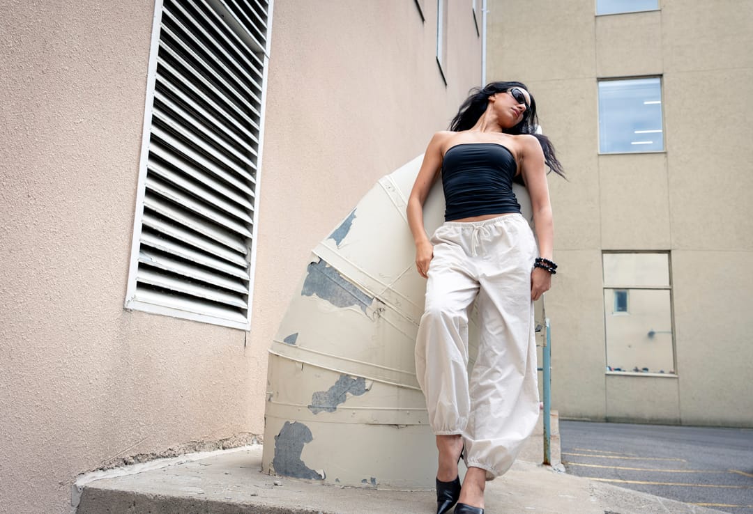 Model leaning against a curved concrete wall beside a louvred vent