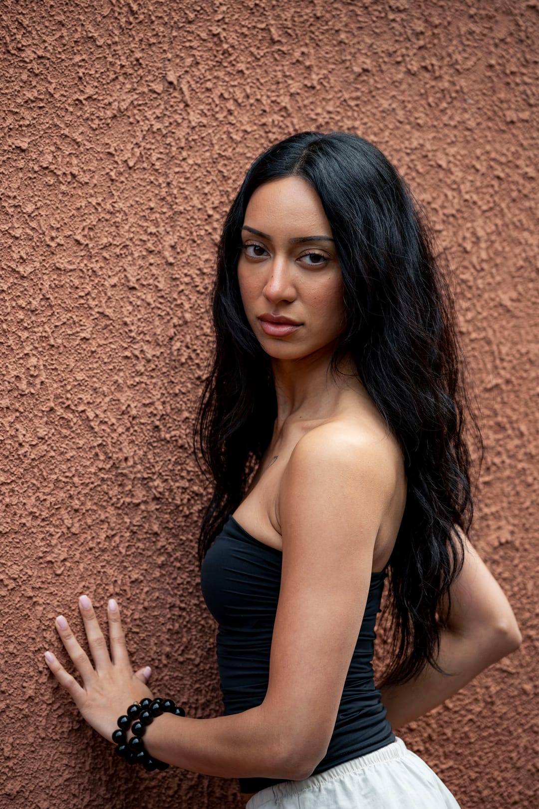 Model with long dark hair and one hand pressed to a terracotta wall