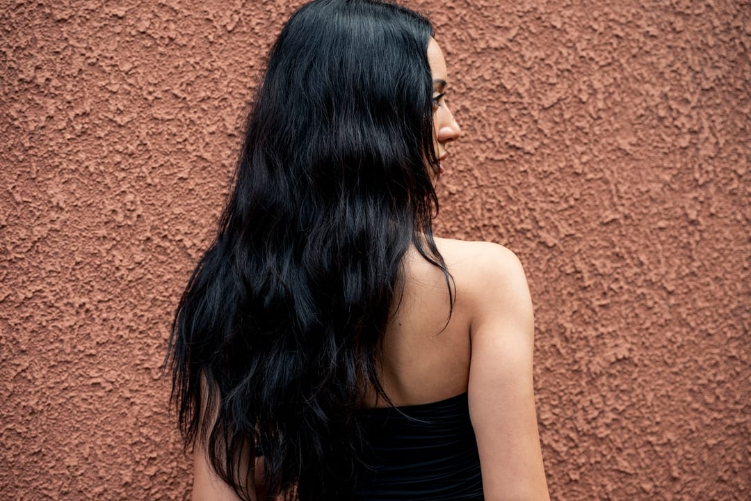 Model seen from behind, long dark hair against a terracotta wall