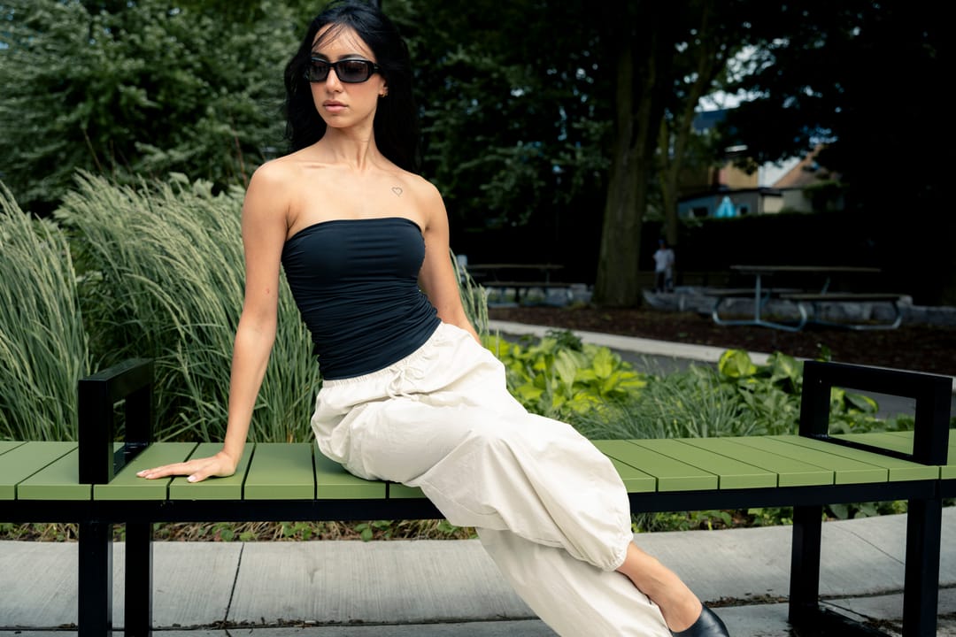 Model in sunglasses seated on a green park bench