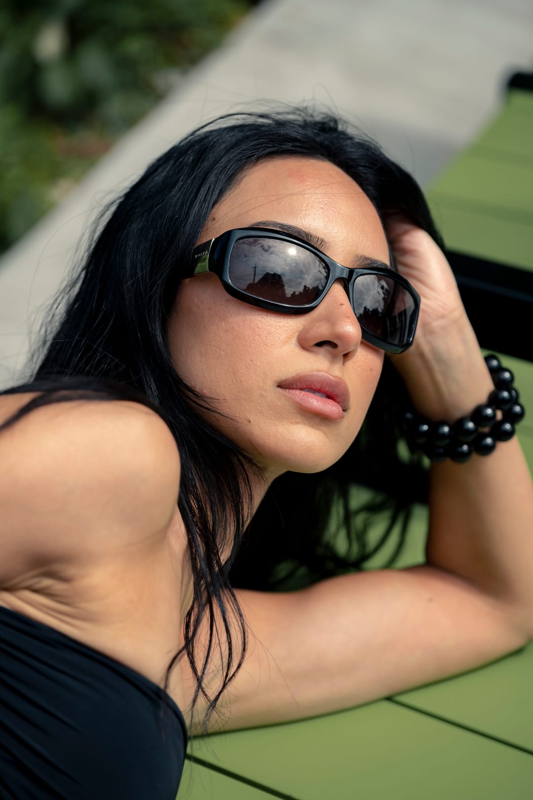 Close portrait of a model in sunglasses resting their head on an arm outdoors