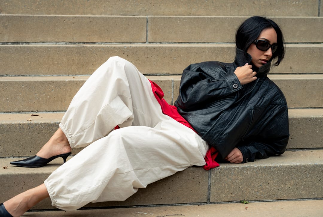 Model in a leather jacket and cream trousers reclining on stone steps