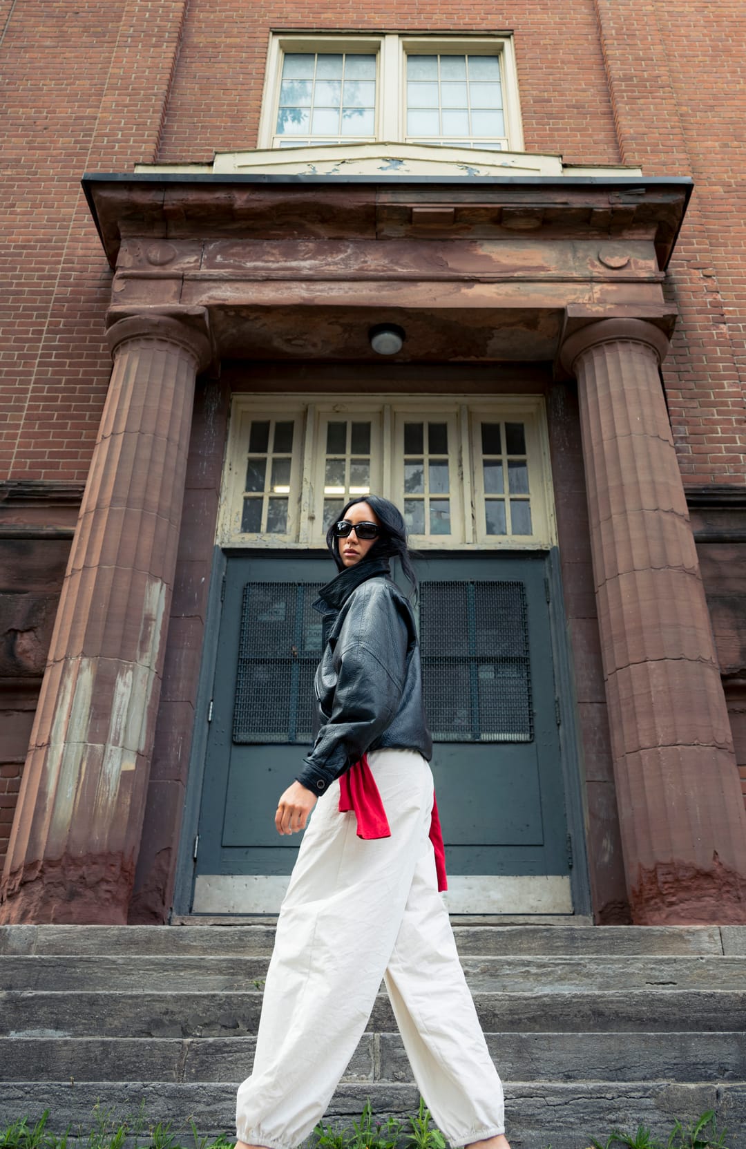 Model walking across the front of a brick building with columns and a green door