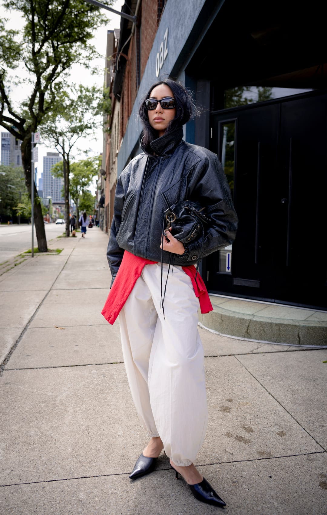 Model in a cropped leather jacket and pointed flats walking along a city sidewalk