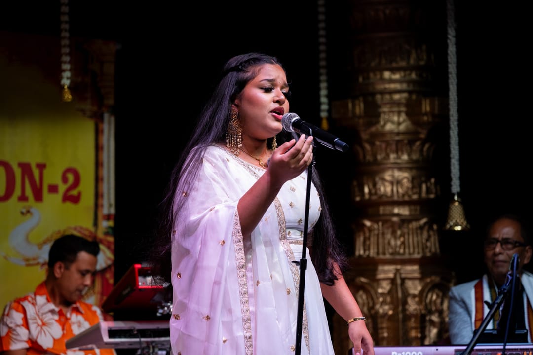 Vocalist singing into a microphone on a stage with carved wooden pillars