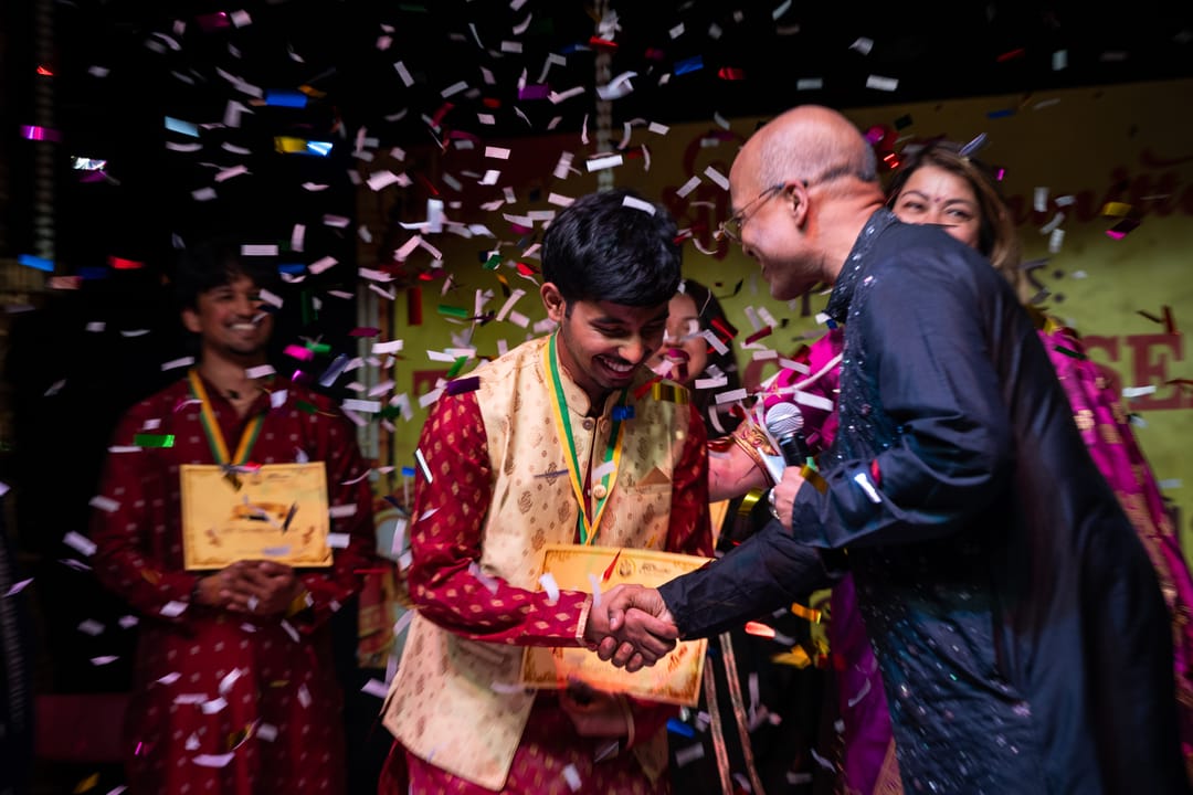 Confetti falling as a boy in a red kurta shakes hands and receives a certificate