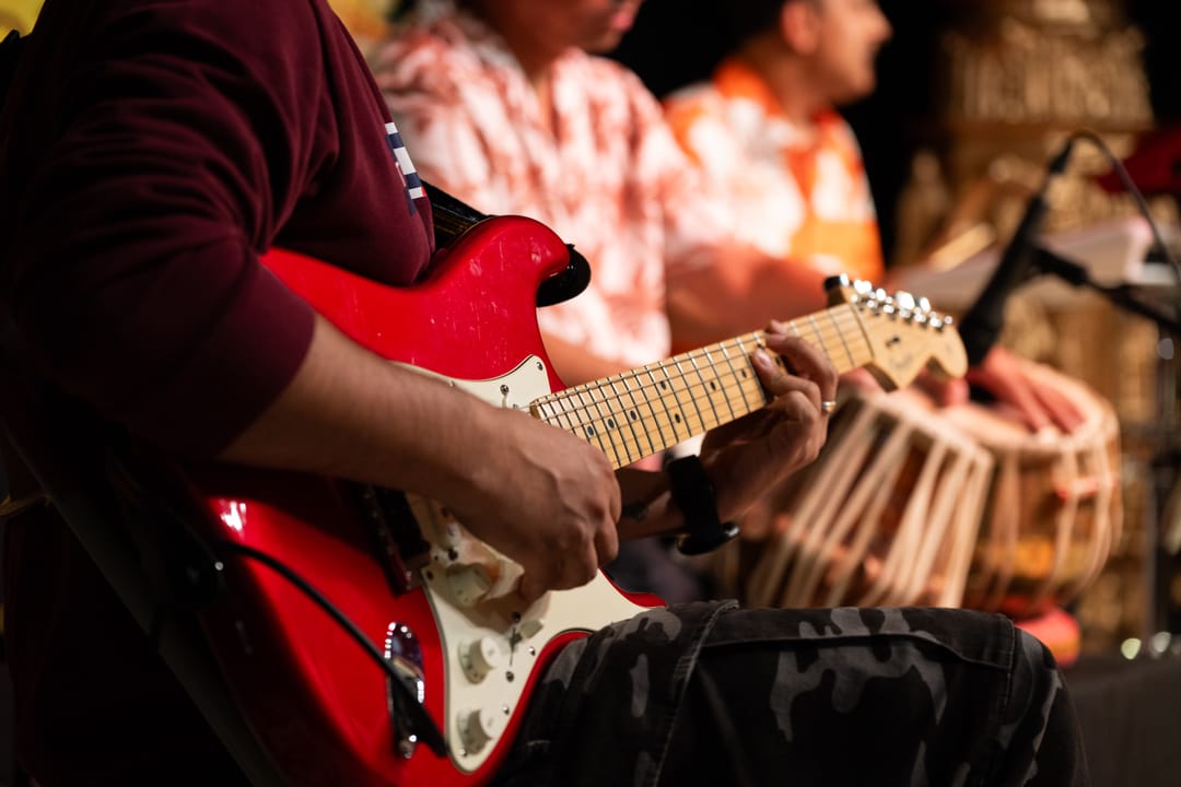 A red electric guitar being played beside a tabla