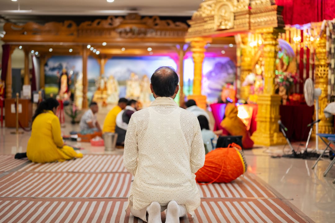 Devotees seated in a temple hall facing an ornate golden shrine