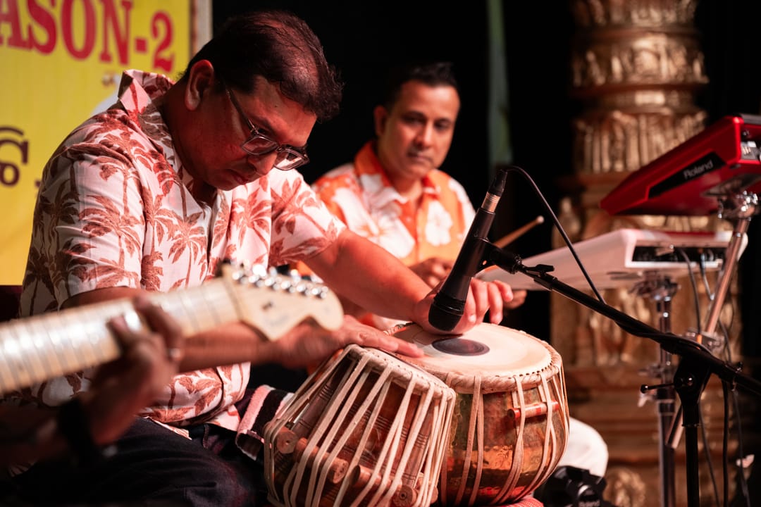 Musicians playing tabla and guitar on stage in patterned shirts