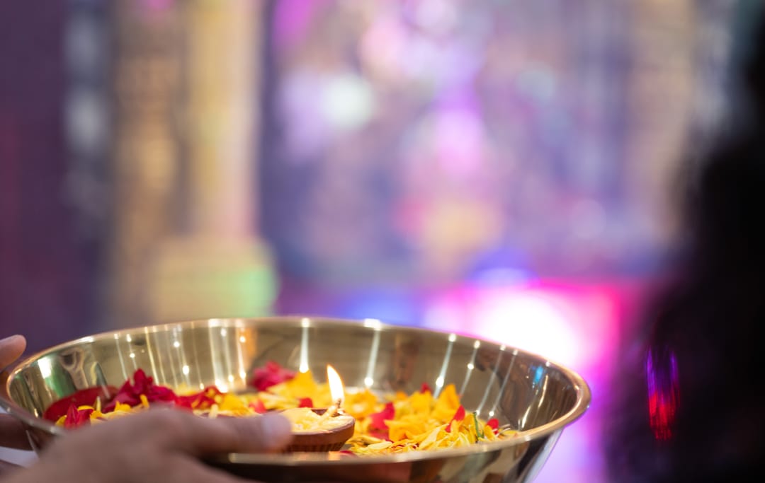 A brass plate holding a lit lamp and flower petals in front of a glowing hall