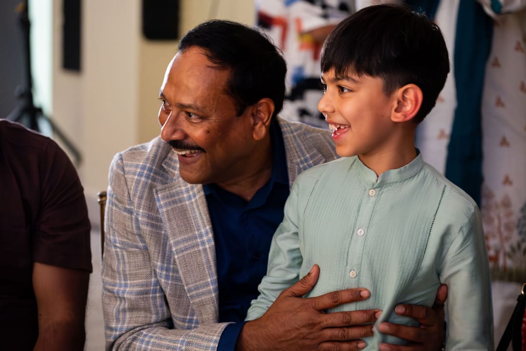 A smiling man in a blazer holding a boy in a green kurta