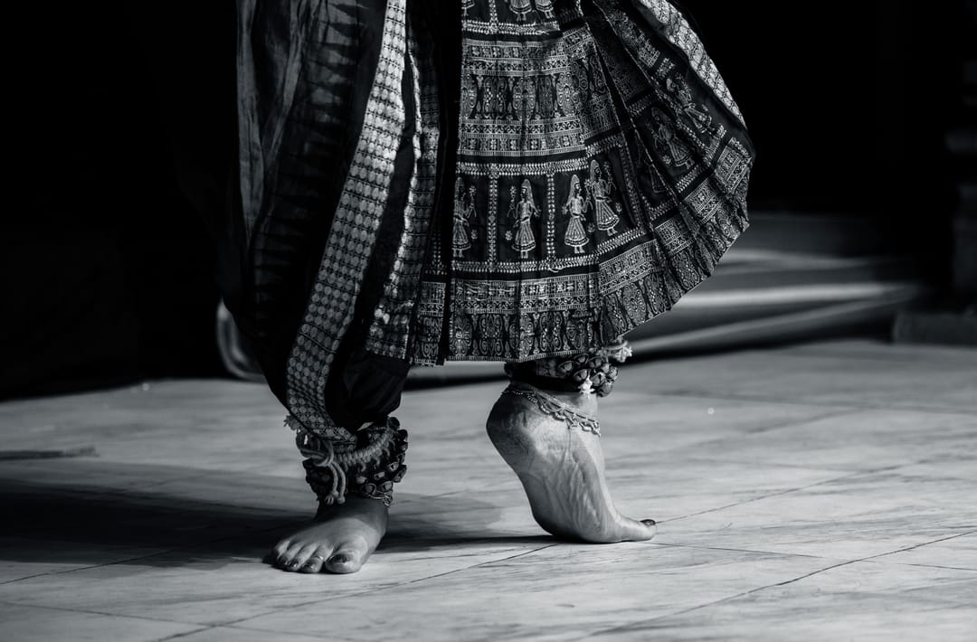 Black and white detail of a dancer’s feet in a patterned skirt on a stage floor