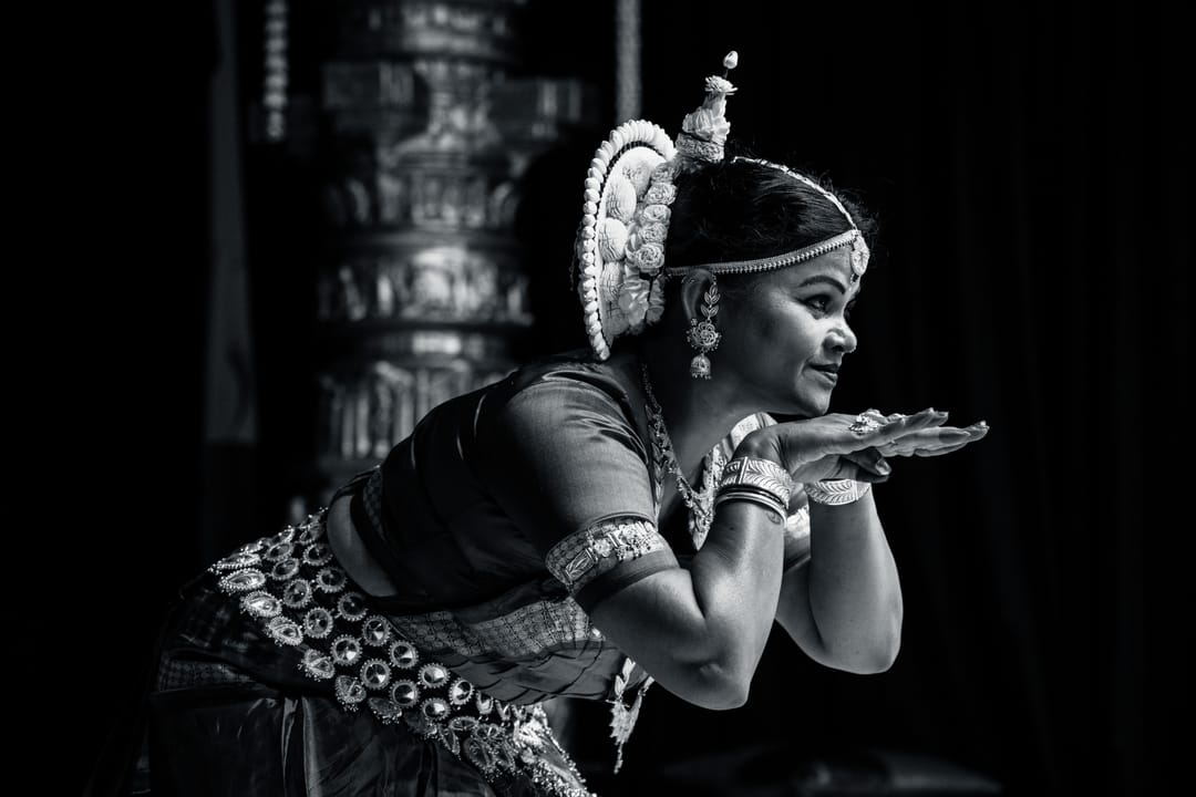 Black and white image of a dancer with cupped hands beside a carved pillar