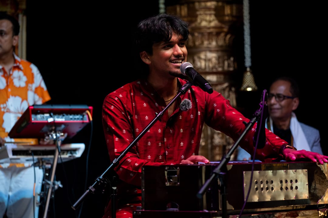 Singer in a red kurta performing with a harmonium on stage