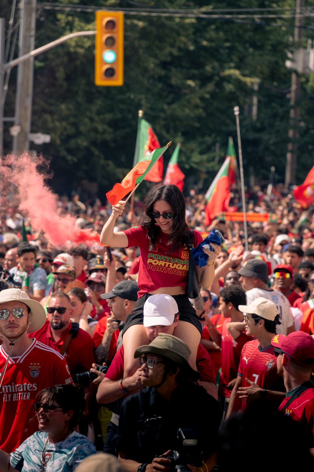 A woman on shoulders in a crowd of red-shirted Portugal fans, waving a flag beside red smoke