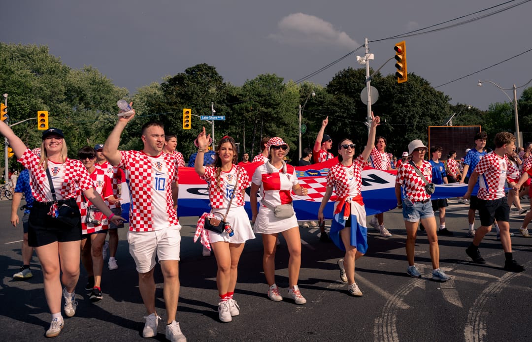 Croatia supporters in checkered shirts marching down the street behind a flag