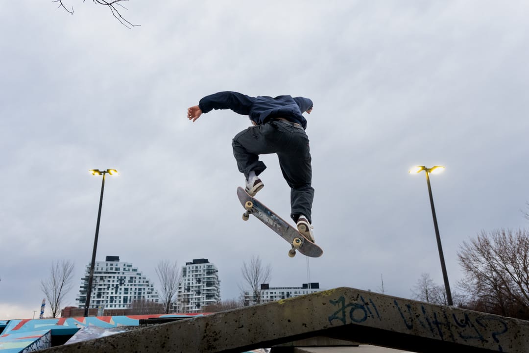 A skateboarder in the air against a cloudy sky, apartment towers behind