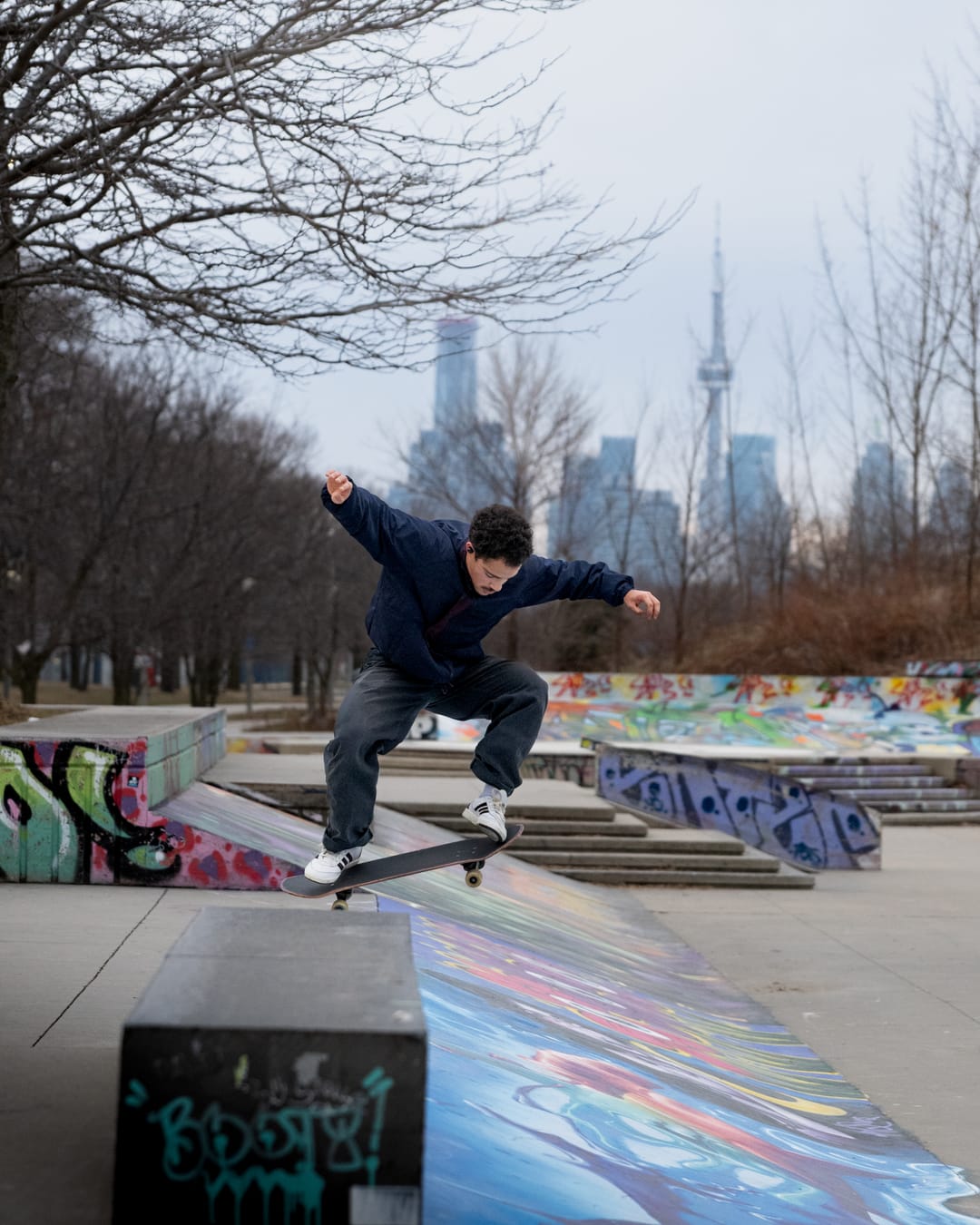 A skateboarder jumping a ledge with the Toronto skyline and CN Tower in the distance