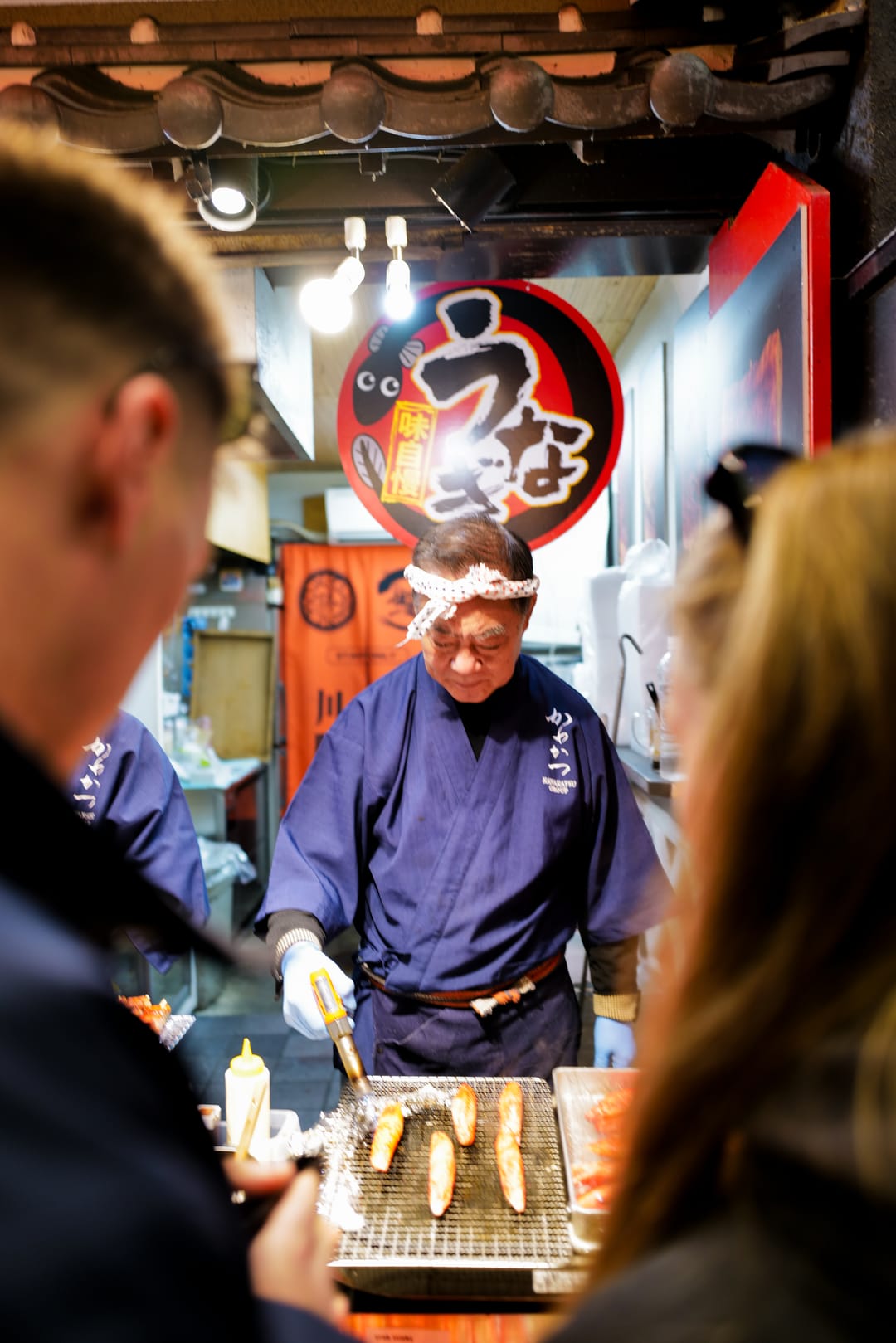 A street food vendor grilling skewers at a lantern-lit stall, customers in the foreground