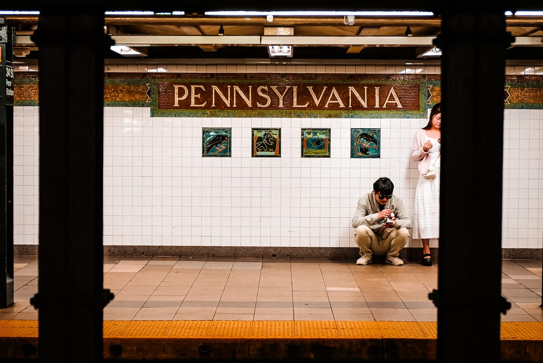 A person crouching on a subway platform beneath a Pennsylvania station sign